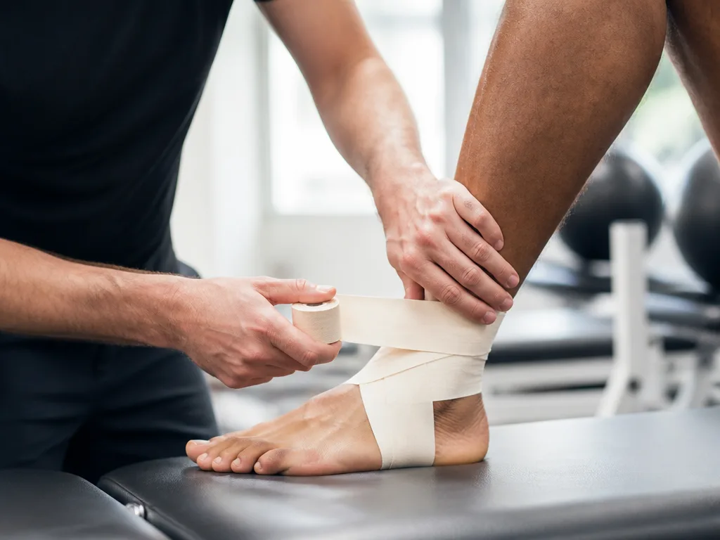 Närbild på händer som tejpar en fotled med sporttejp för extra stöd